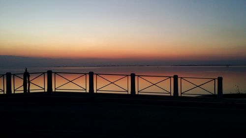 Silhouette bridge over sea against sky during sunset