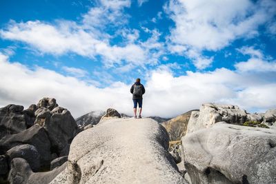 Rear view of man standing on rocks against sky