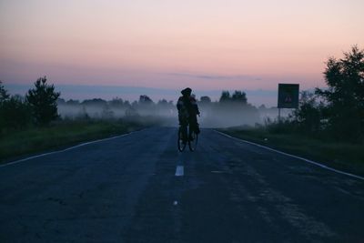 Rear view of woman riding bicycle on road against sky