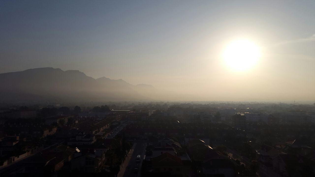 cityscape, building exterior, city, architecture, built structure, crowded, sun, high angle view, aerial view, sunset, residential district, sky, landscape, sunlight, residential building, mountain, residential structure, outdoors, sunbeam, clear sky