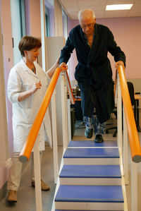 Physical therapist assisting senior man in climbing steps at nursing home