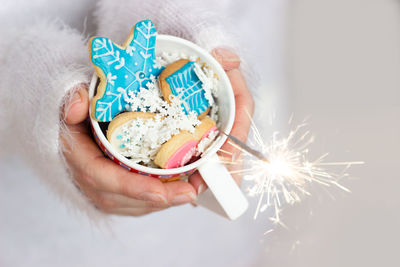 Midsection of woman holding sweet food and sparkler at home
