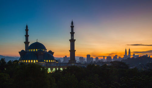 Illuminated buildings in city against sky during sunset