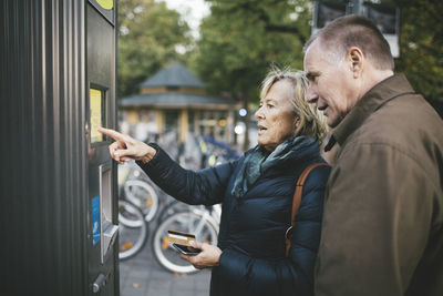 Senior man with woman making payment through credit card at bike rental station
