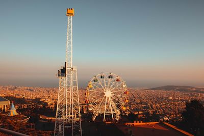 Ferris wheel by illuminated buildings against sky during sunset