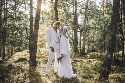 Bride looking at groom while standing amidst trees in forest on wedding day