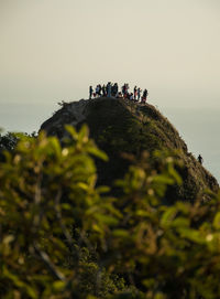 Low angle view of people standing on cliff against sky