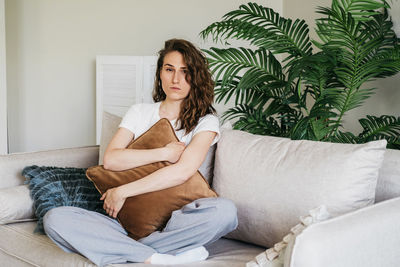 A sad woman sits on a sofa at home hugging a pillow.