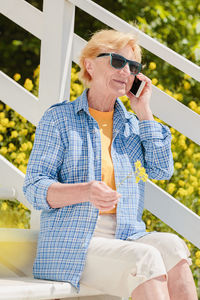 Mature woman sitting alone on the terrace of beach cafe and using mobile phone
