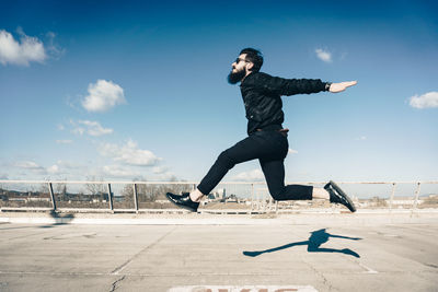 Full length of man jumping in city against sky