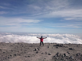 Rear view of man with arms outstretched standing against cloudy sky