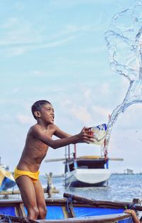 Full length of shirtless boy in water against sky