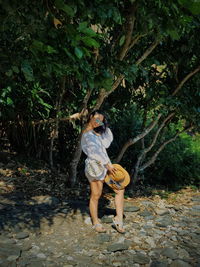 Side view of young woman wearing sunglasses standing against trees in forest