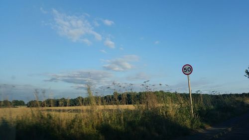 Road sign on field against cloudy sky