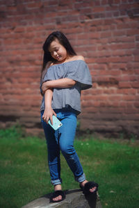 Portrait of smiling girl standing against brick wall