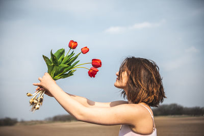 Woman holding red flowering plant against sky