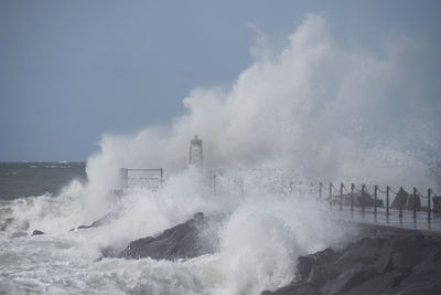 Waves splashing on rocks against sky