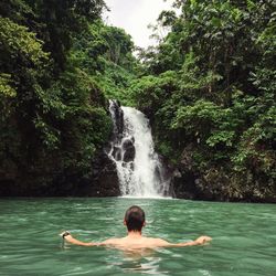 Man swimming in river against waterfall