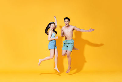 Full length of a smiling young woman against yellow background