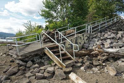 Wooden footbridge over rocks in forest against sky