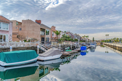 Boats moored in canal by houses against sky