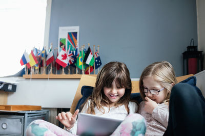 Smiling friends using digital tablet while sitting on sofa in school