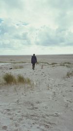 Man walking on sand at beach against sky