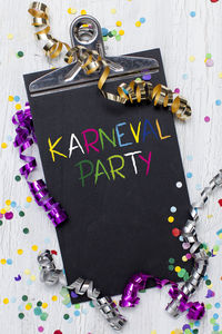Directly above shot of karneval party text on clipboard with confetti at table