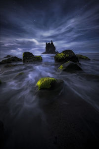 Rocks on beach against sky at dusk