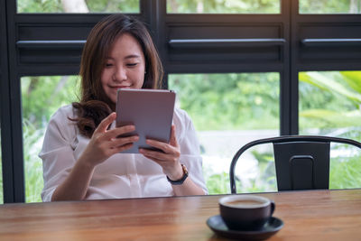 Woman using digital tablet by coffee cup while sitting on table