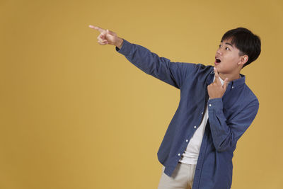 Young man looking away while standing against yellow background