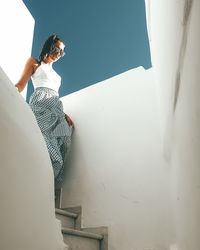 Young woman sitting on staircase against wall