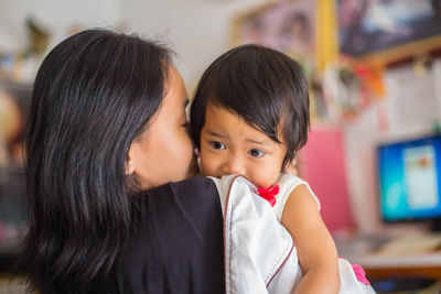 Mother carrying daughter while standing at home