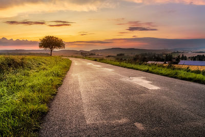 Road by trees against sky during sunset