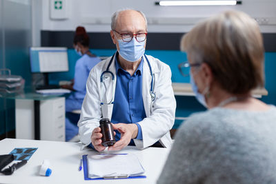 Doctor wearing mask showing medicine to patient