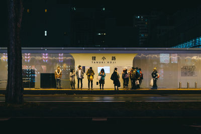 People waiting at illuminated railroad station platform at night