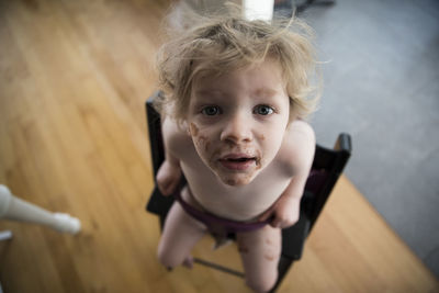 Messy faced toddler sits in high chair and looks up into camera