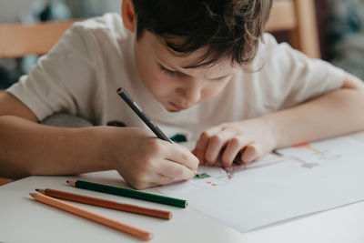 The boy draws with pencils at the kitchen, closeup. high quality photo