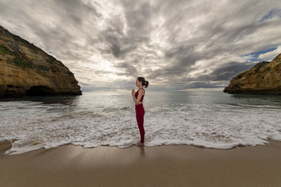 Woman meditating by the sea with prayer hands, dramatic sky and waves.