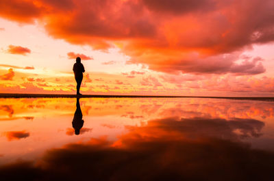 Silhouette man standing on shore against orange sky