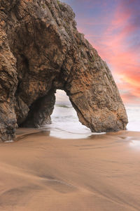 Rock formation on beach against sky during sunset