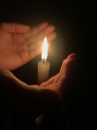 Close-up of hand holding lit candle against black background. bright hands and glowing wax candle in 