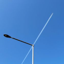 Low angle view of vapor trial over street light against clear blue sky