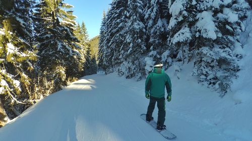 Rear view of man snowboarding amidst trees