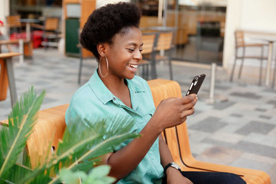 Smiling young woman using smart phone while sitting at cafe