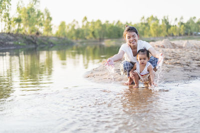 Happy family mother and little daughter playing in the water on the beach on a sunny day.