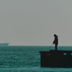 Silhouette man standing by sea against clear sky