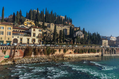 View of buildings by river against blue sky