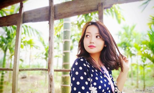 Beautiful young woman looking away while standing against plants