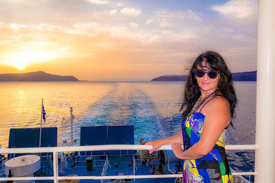 Portrait of woman standing by railing against sea during sunset